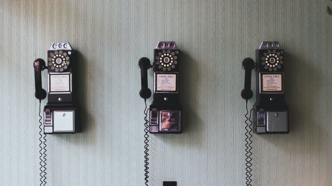 Three vintage rotary payphones mounted on a patterned wall.